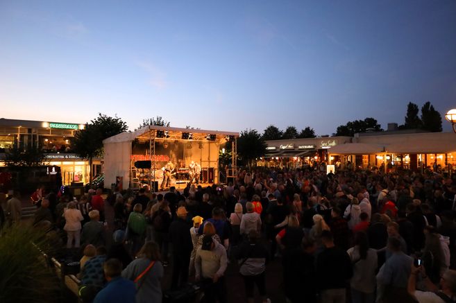 Open-Air-Konzert bei Abenddämmerung mit einer großen Menschenmenge vor der Bühne.