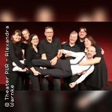 Gruppe von acht Personen in schwarzer Kleidung, eine Person wird horizontal von den anderen getragen.