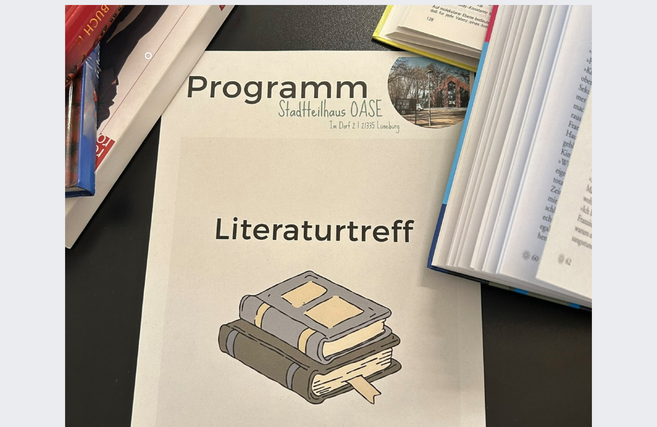 Ein Programmheft mit der Aufschrift 'Literaturtreff' liegt auf einem Tisch, umgeben von geöffneten Büchern.