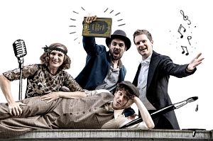 Vier Personen in Retro-Kleidung posieren fröhlich mit einem Mikrofon und einem Buch.