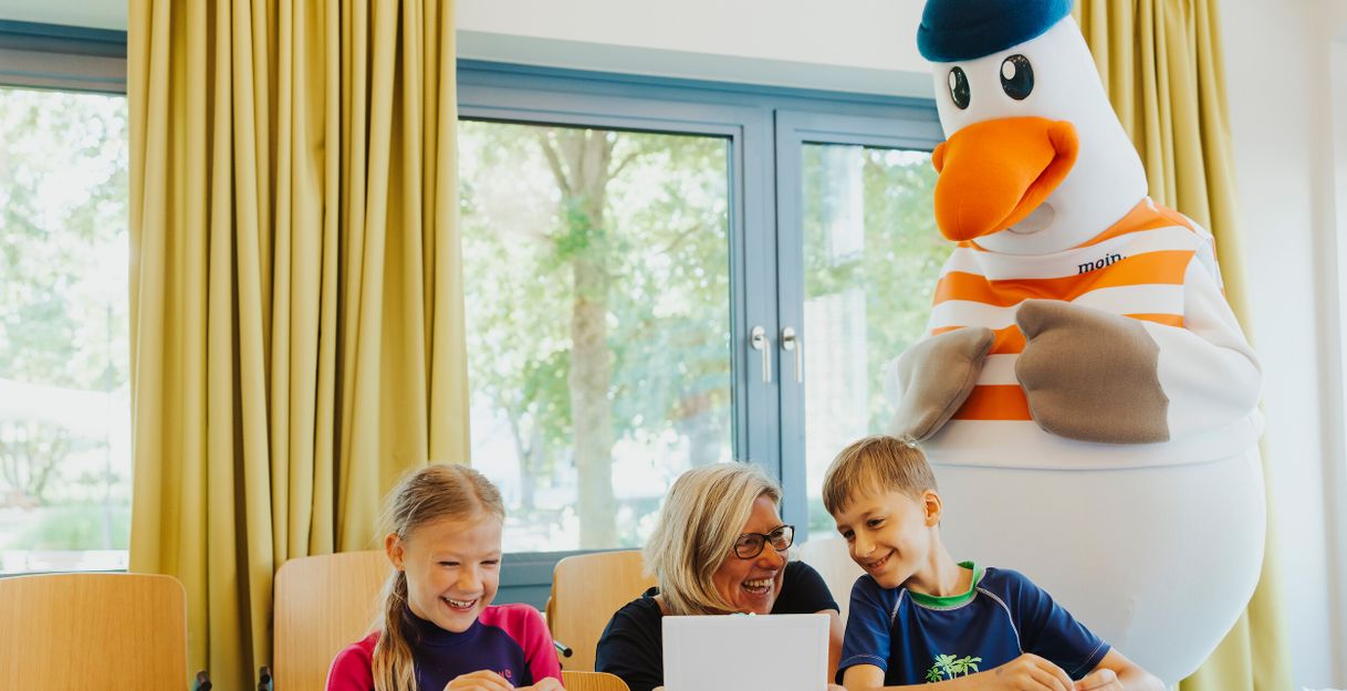 Kinder basteln mit einer Betreuerin, während ein Möwen-Maskottchen zuschaut.