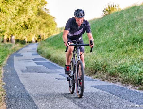Ein Mann auf einem Rennrad fährt auf einem schmalen, asphaltierten Weg durch eine grüne Landschaft.