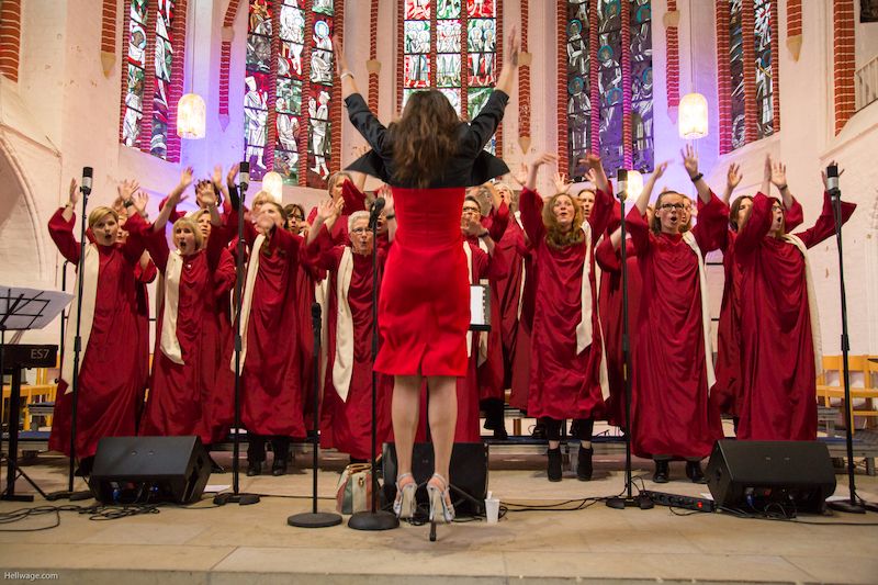 Ein Gospelchor in roten Roben singt in einer Kirche mit bunten Glasfenstern.