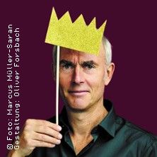 Ein Mann hält eine goldene Papierkrone auf einem Stab vor seinem Kopf.