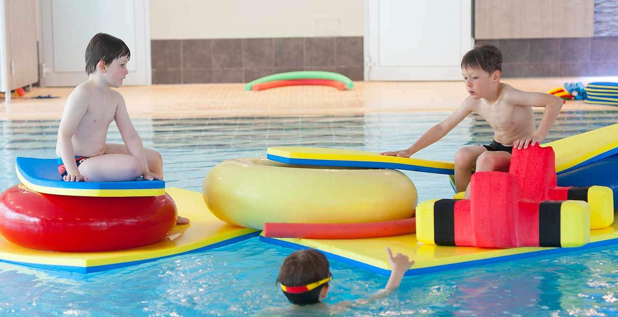 Kinder spielen auf bunten Schwimmplattformen in einem Hallenbad.