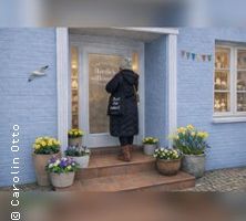 Eine Person steht vor einem blauen Gebäude mit Blumen und Dekorationen.