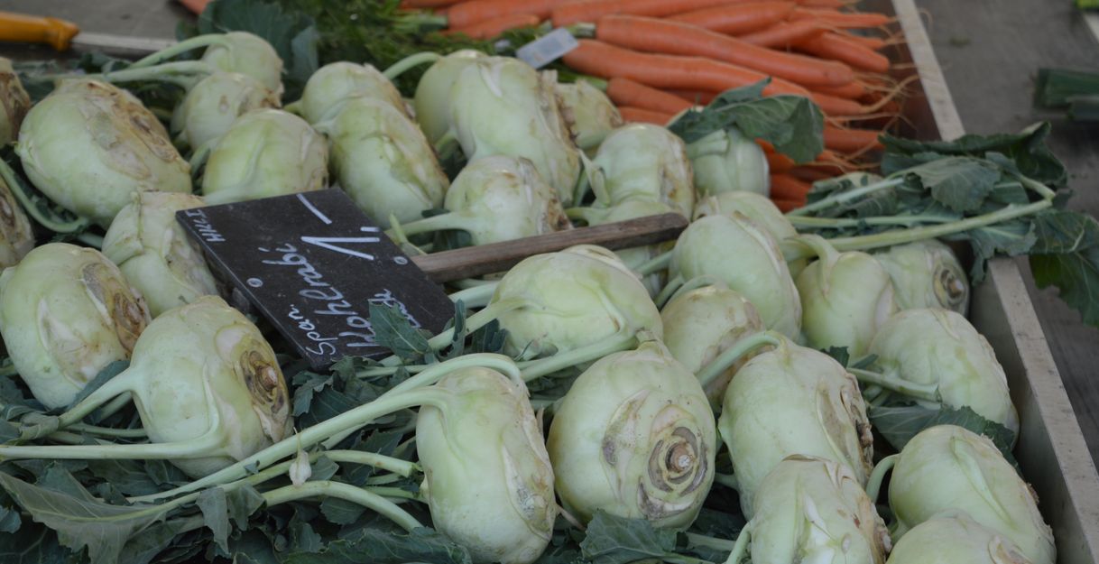 Nahaufnahme von Kohlrabi und Karotten auf einem Marktstand.