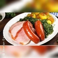 Ein Teller mit Grünkohl, Kassler, Mettwurst und Bratkartoffeln.