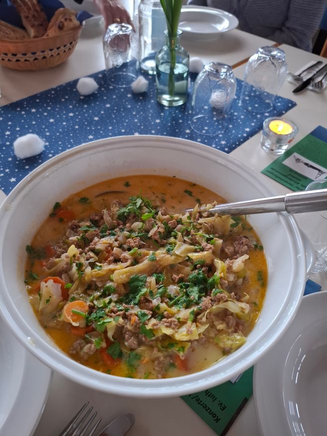 Ein Tisch mit einer großen Schüssel Eintopf, umgeben von Tellern, Gläsern und einer Kerze.