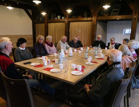 Eine Gruppe älterer Menschen sitzt um einen Tisch in einem Raum mit Holzbalken.