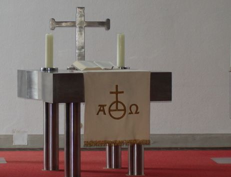 Ein moderner Altar mit einem Kreuz, einer Bibel und Kerzen auf einem roten Teppich.