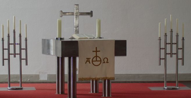Ein moderner Altar mit einem Kreuz, Kerzen und einem Tuch mit christlichen Symbolen.