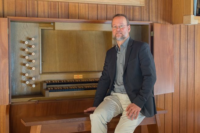 Ein Mann sitzt auf einer Orgelbank vor einer hölzernen Orgel.