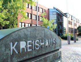 Ein Schild mit der Aufschrift 'Kreishaus' vor einem modernen Backsteingebäude mit Glasfassade.