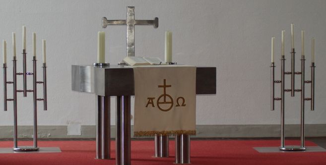 Ein moderner Altar mit einem Kreuz, einer Bibel und Kerzen auf einem roten Teppich.
