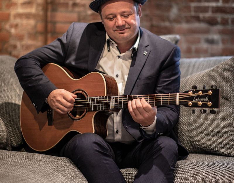Ein Mann in einem Anzug spielt Gitarre auf einem Sofa.