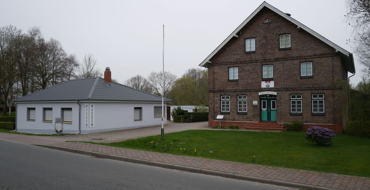 Ein kleines Museum und ein größeres Backsteingebäude an einer Straße.