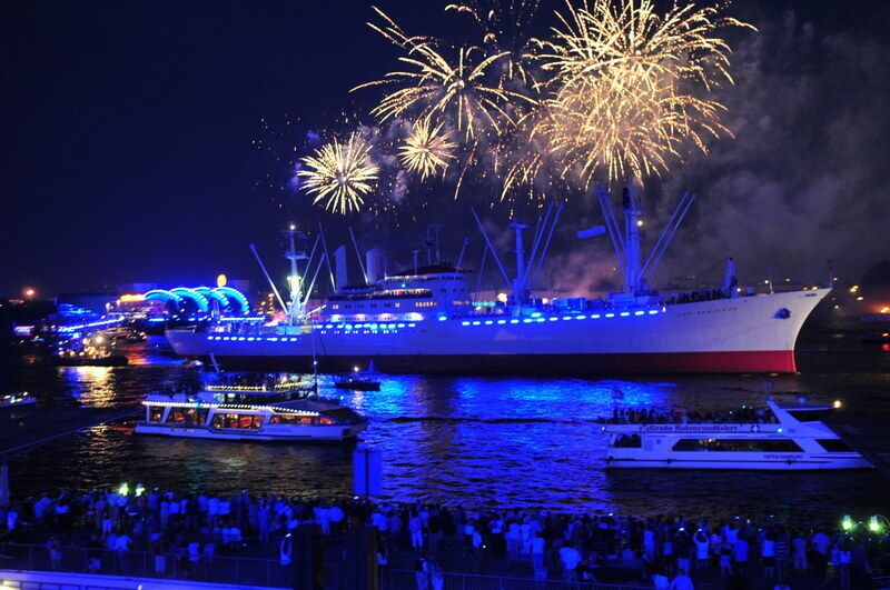 Beleuchtetes Schiff im Hamburger Hafen mit Feuerwerk am Nachthimmel.